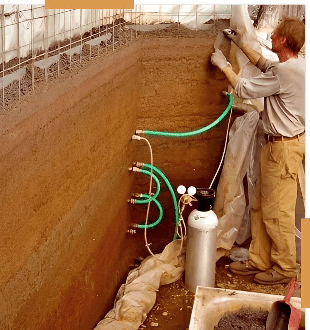 Man constructing earthen wall with hoses attached.